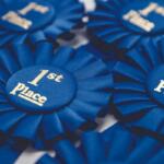 Blue first-place award ribbons with satin folds and gold text reading '1st Place' on round centers