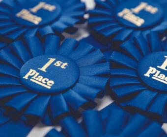 Blue first-place award ribbons with satin folds and gold text reading '1st Place' on round centers