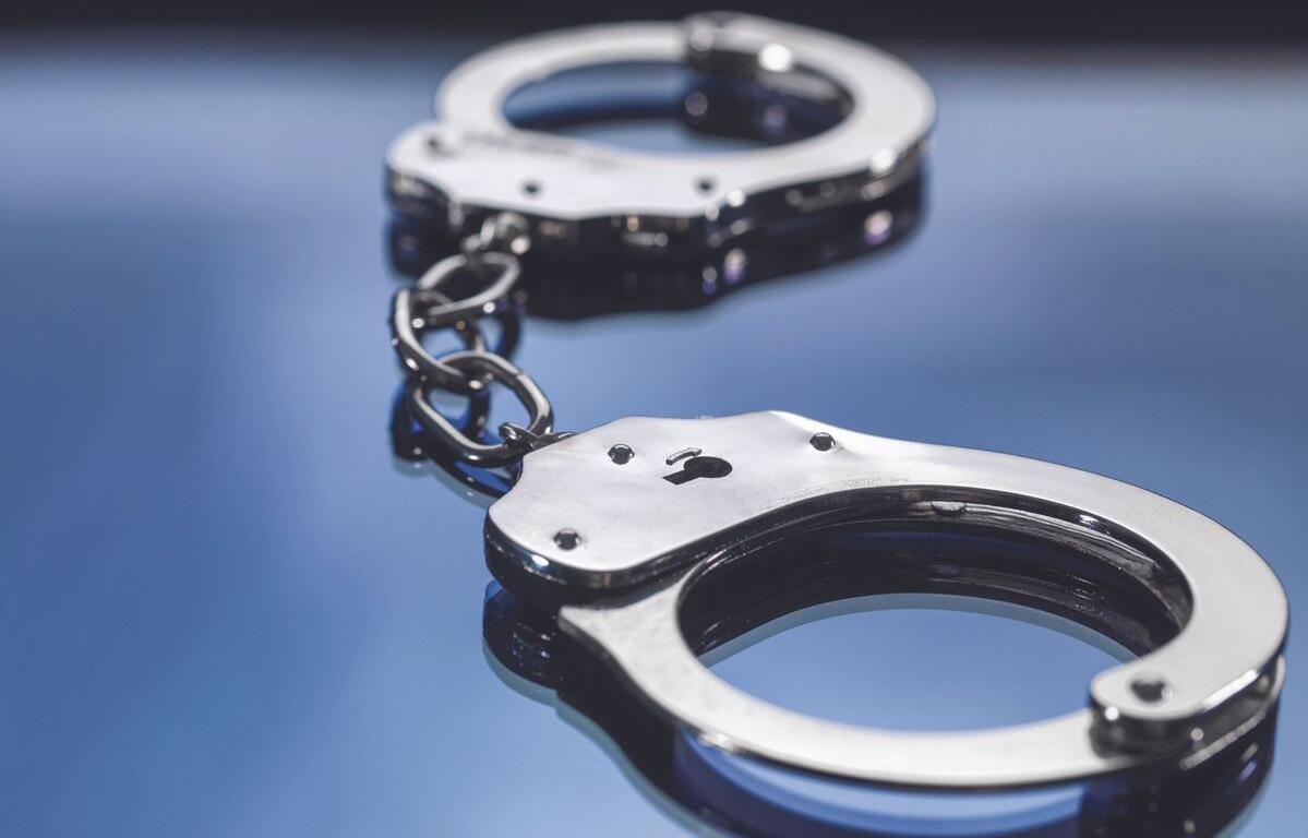 Silver handcuffs linked together on a reflective blue surface, close-up view.