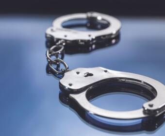 Silver handcuffs linked together on a reflective blue surface, close-up view.