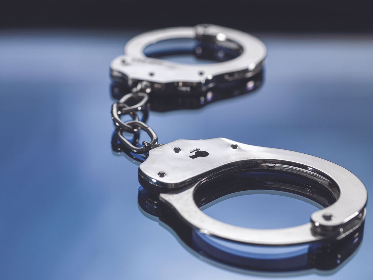 Silver handcuffs linked together on a reflective blue surface, close-up view.