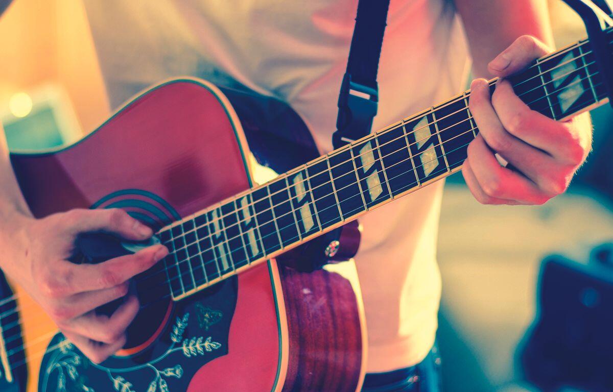 Close-up of a person’s hands playing an acoustic guitar, fingers on the fretboard and strumming near the soundhole.