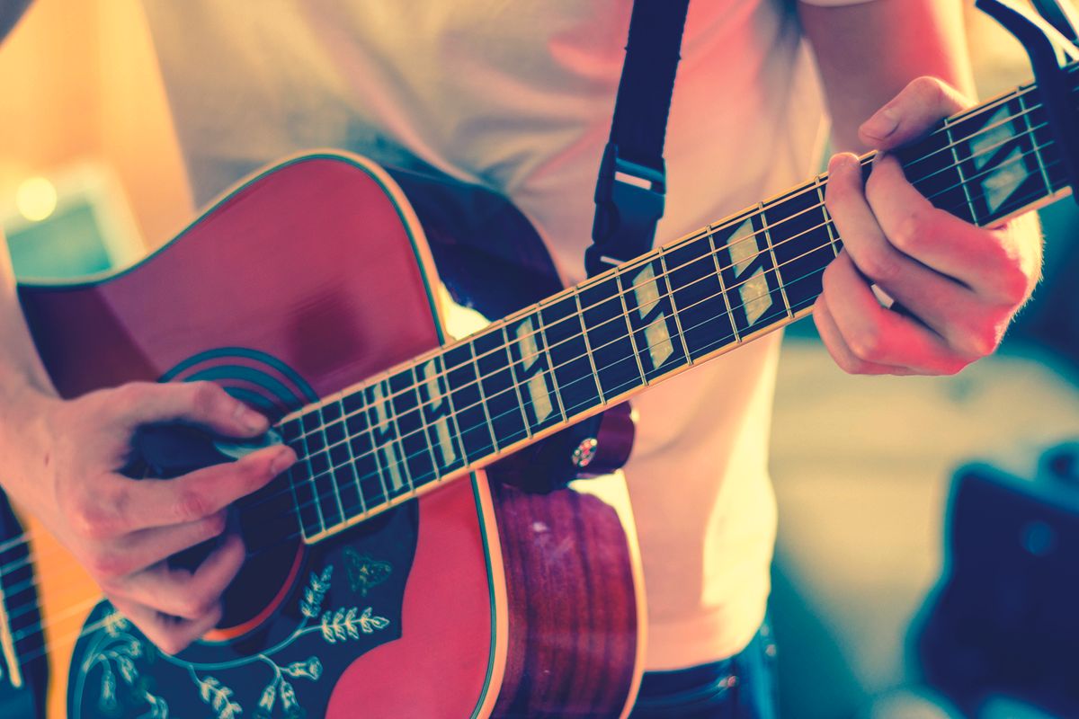 Close-up of a person’s hands playing an acoustic guitar, fingers on the fretboard and strumming near the soundhole.