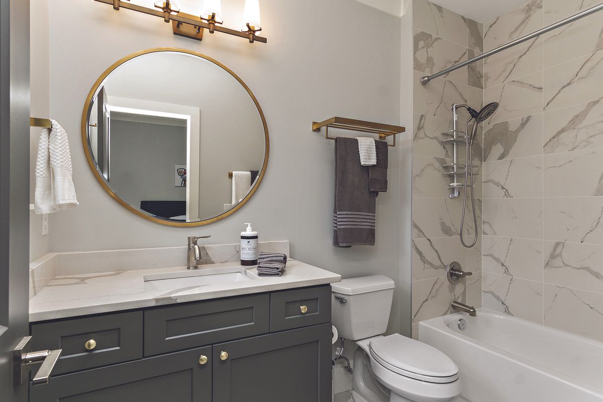 Modern bathroom vanity with dark cabinet, marble countertop, round gold-framed mirror, and soap dispenser.