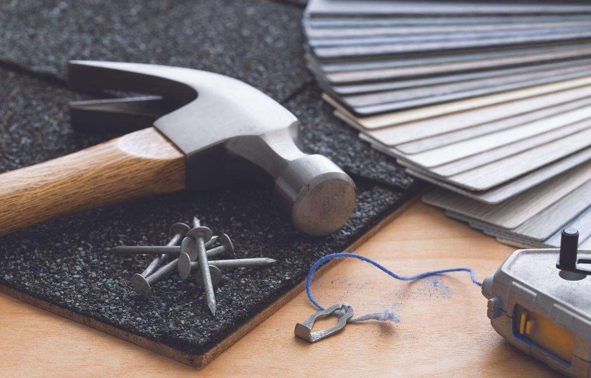 Hammer and nails on a textured mat with color swatches, blue string, and a small metal heart charm on a wooden work surface.