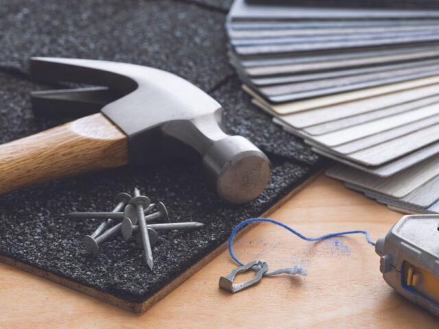 Hammer and nails on a textured mat with color swatches, blue string, and a small metal heart charm on a wooden work surface.
