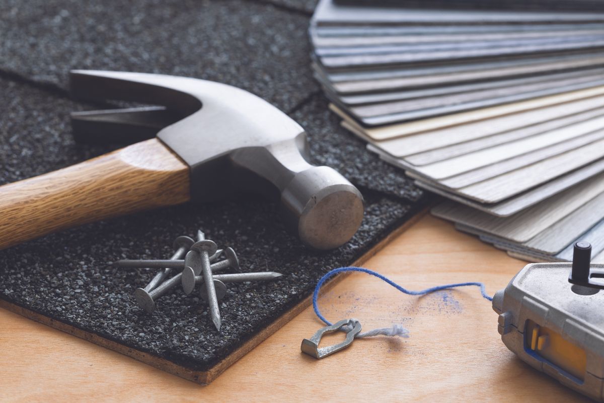 Hammer and nails on a textured mat with color swatches, blue string, and a small metal heart charm on a wooden work surface.