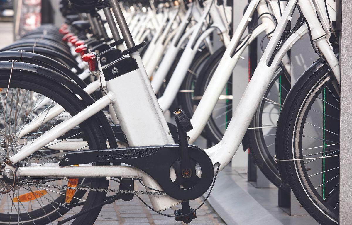 Row of white bicycles docked at a bike-share station, foreground shows the crank and chain close up