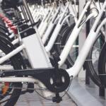 Row of white bicycles docked at a bike-share station, foreground shows the crank and chain close up