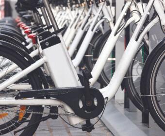 Row of white bicycles docked at a bike-share station, foreground shows the crank and chain close up