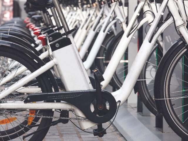 Row of white bicycles docked at a bike-share station, foreground shows the crank and chain close up
