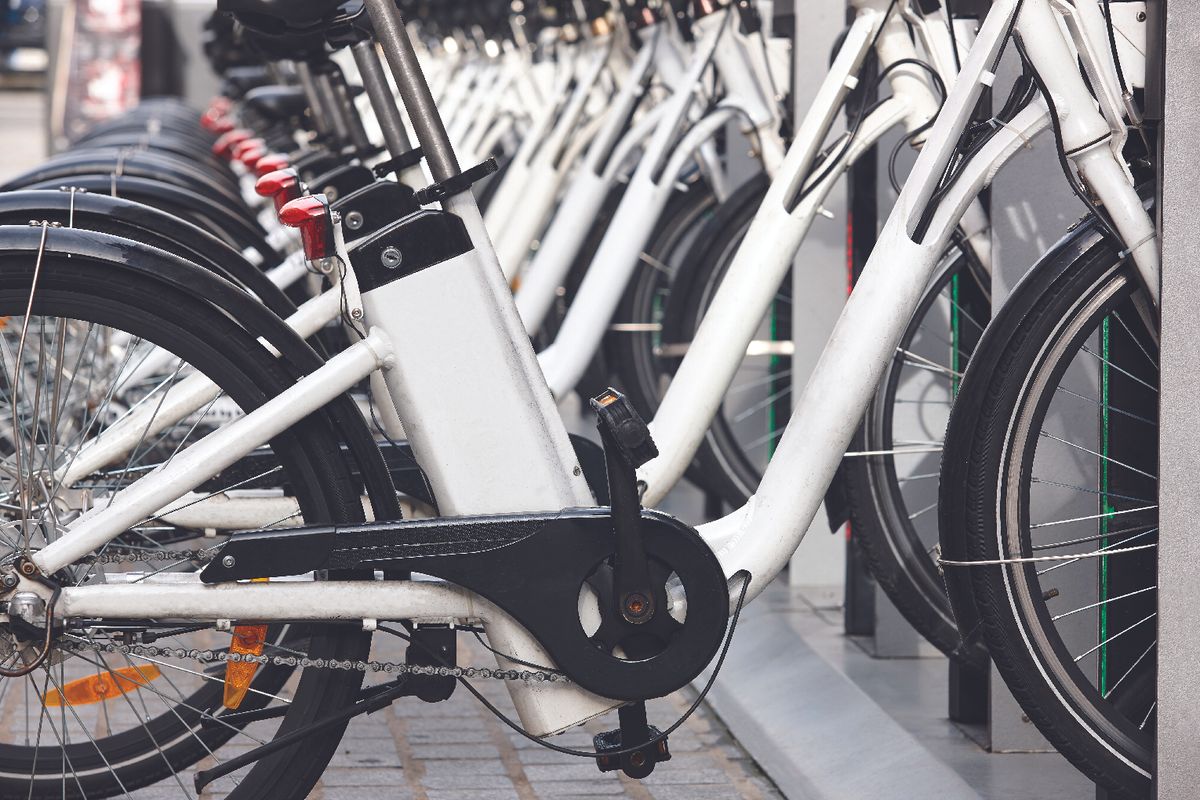 Row of white bicycles docked at a bike-share station, foreground shows the crank and chain close up