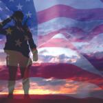 Silhouette of a soldier saluting with a rifle, overlaid on a waving American flag at sunset/dusk Вост.