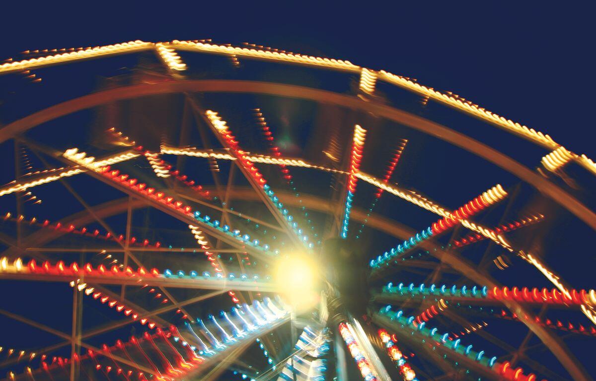 Blurred ferris wheel at night with multicolored lights radiating from the center around a bright glow at the hub.