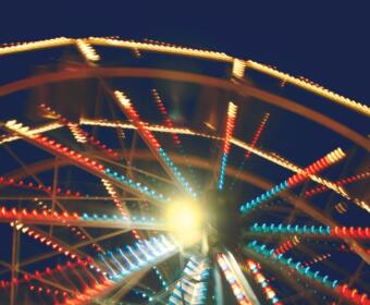 Blurred ferris wheel at night with multicolored lights radiating from the center around a bright glow at the hub.