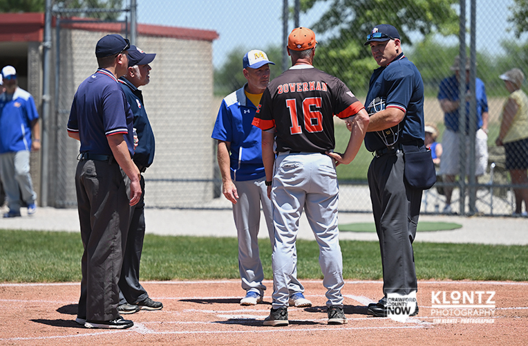 Baseball players and umpires gather on the infield for a discussion during a game, with a player wearing number 16 at center.