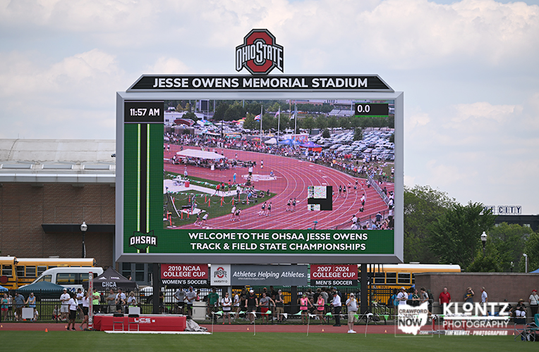 Electronic scoreboard at Jesse Owens Memorial Stadium displaying the track & field state championships, with the Ohio State logo on top and a crowd in the background.