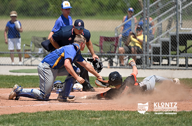 Baserunner slides into home plate as the catcher reaches to tag him, with an umpire and teammates watching nearby.
