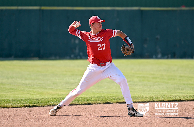 Right-handed baseball pitcher in a red uniform (number 27) delivering a pitch from the mound on a sunny field.