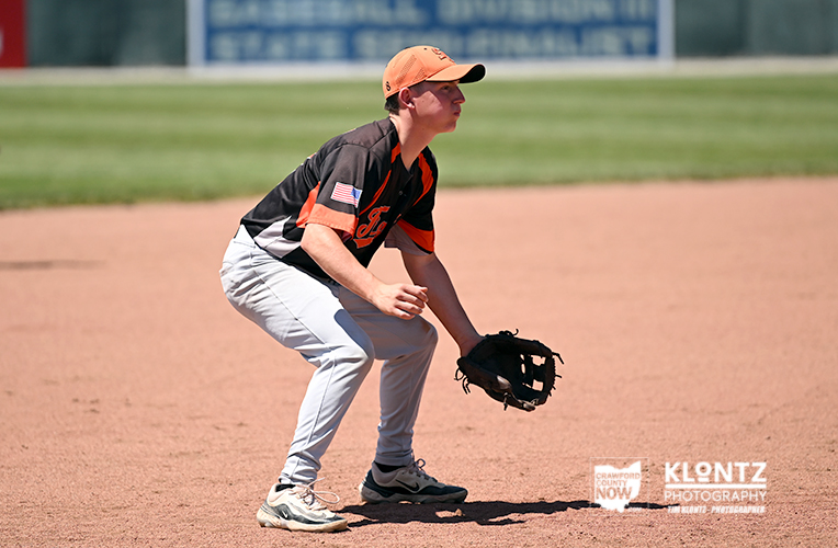 Youth baseball player crouching in fielding position with glove ready to field a ground ball on a dirt infield.