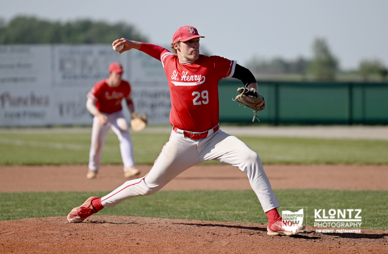Baseball pitcher in a red St. Henry jersey #29 delivering a pitch on the mound during a game.