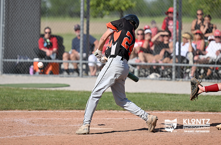 Baseball batter in black-orange jersey swinging at a pitch during a game, crowd behind the fence watching.
