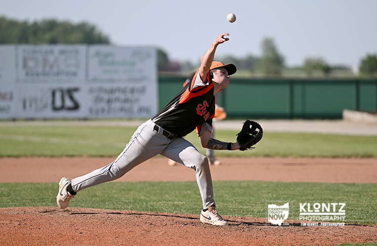 Baseball pitcher in black-and-orange uniform throwing a pitch on the mound as the ball sails through the air