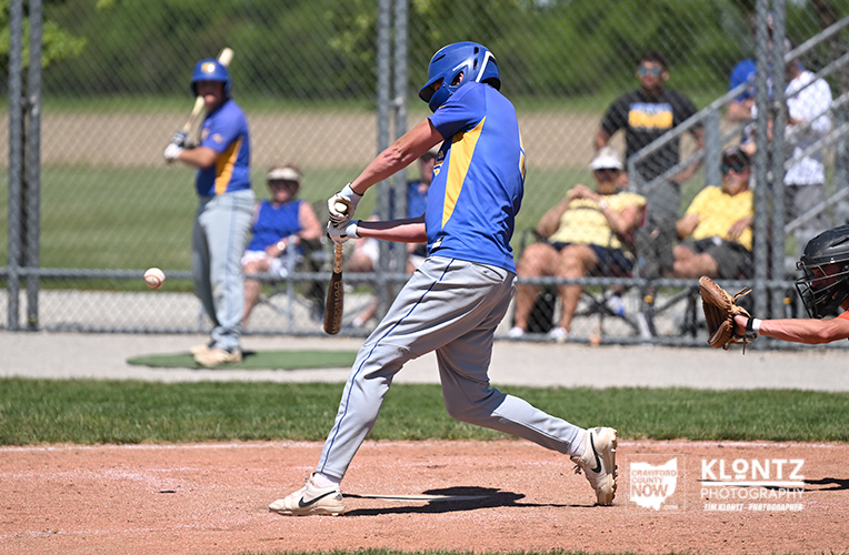 Baseball batter in blue and yellow swings at a pitched ball on a sunny field.