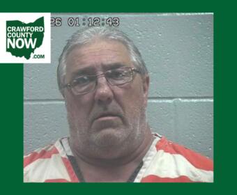 Mugshot of a middle-aged man with gray hair and glasses in orange-and-white jail clothes, against a gray wall; Crawford County Now logo in the corner.
