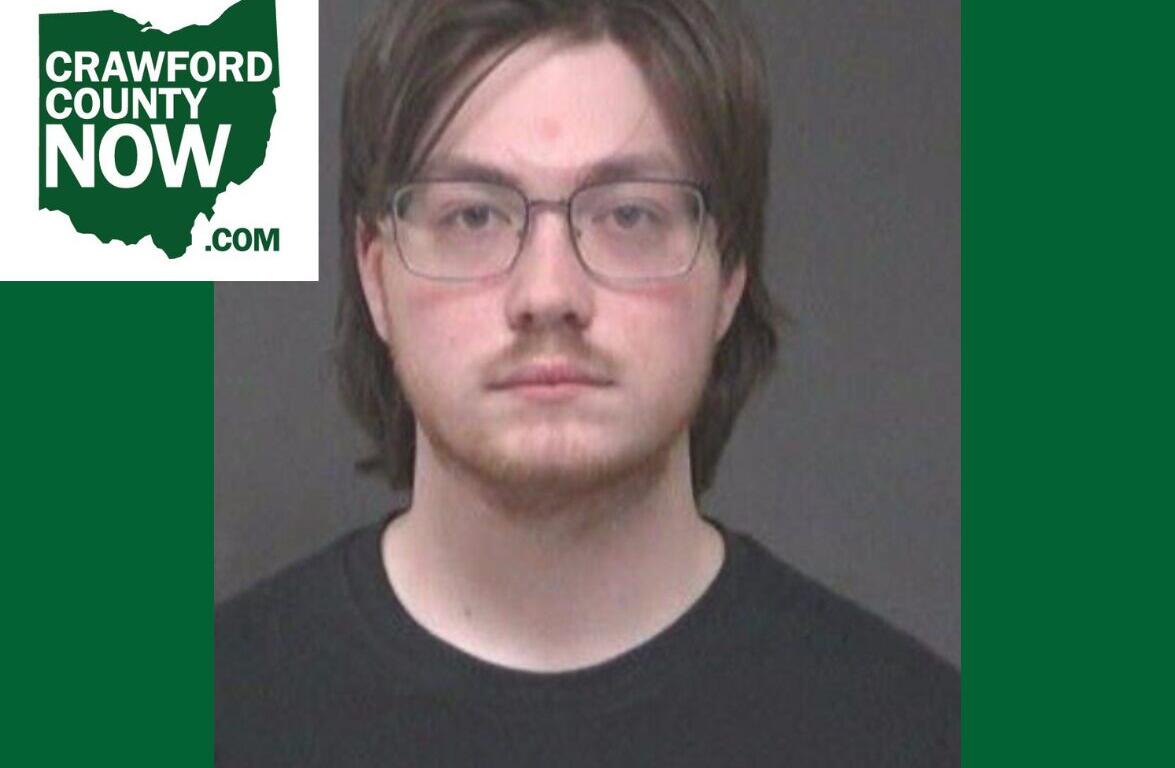 Mugshot-style portrait of a young man with glasses, dark hair, and a black shirt; Crawford County Now logo overlaps the image.