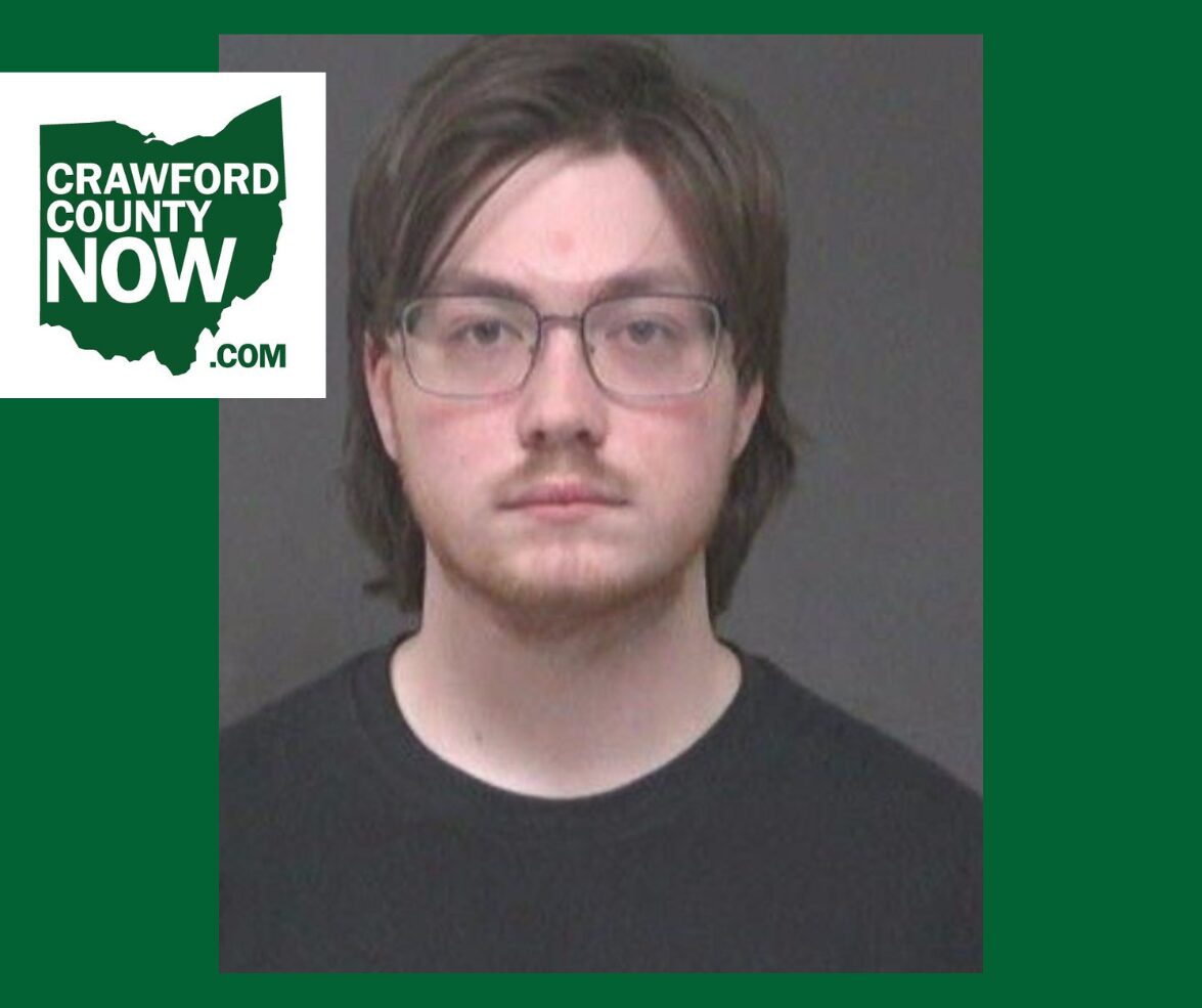 Mugshot-style portrait of a young man with glasses, dark hair, and a black shirt; Crawford County Now logo overlaps the image.