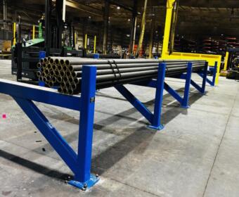 Blue industrial rack holding bundled steel pipes in a factory warehouse, with a forklift and yellow support columns in the background