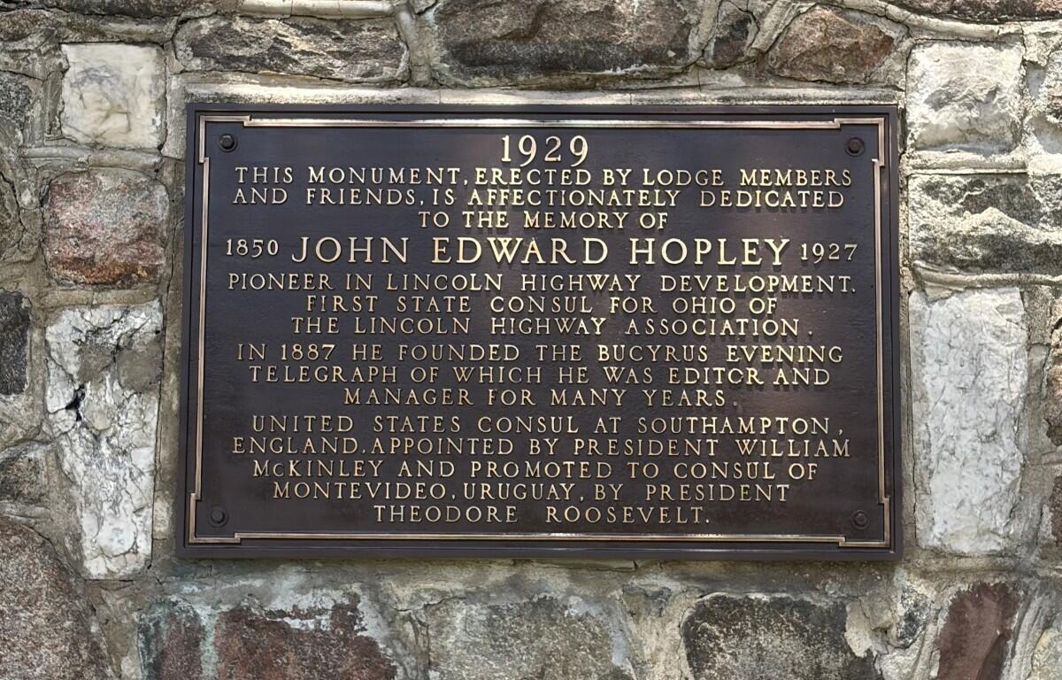 Bronze commemorative plaque mounted on a rough stone wall honoring John Edward Hopley and his contributions to Lincoln Highway, dated 1929 with biographical details etched in gold lettering.
