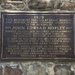 Bronze commemorative plaque mounted on a rough stone wall honoring John Edward Hopley and his contributions to Lincoln Highway, dated 1929 with biographical details etched in gold lettering.