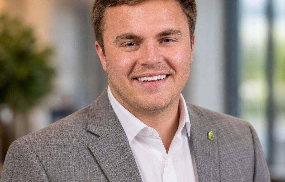 Smiling man in a gray blazer and white shirt in a bright office setting.