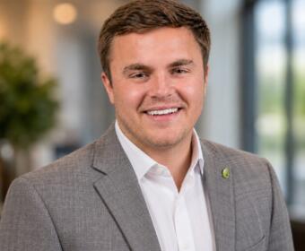 Smiling man in a gray blazer and white shirt in a bright office setting.