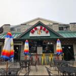 Outdoor seating in front of a casual restaurant with colorful striped umbrellas and metal tables and chairs.