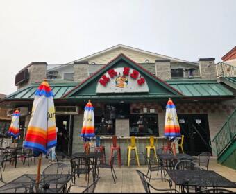 Outdoor seating in front of a casual restaurant with colorful striped umbrellas and metal tables and chairs.