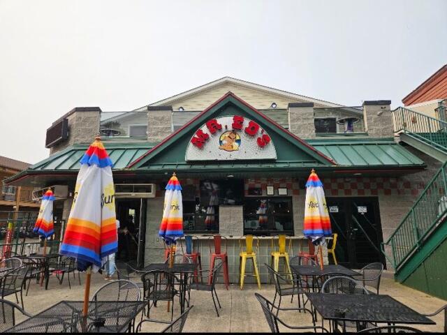 Outdoor seating in front of a casual restaurant with colorful striped umbrellas and metal tables and chairs.