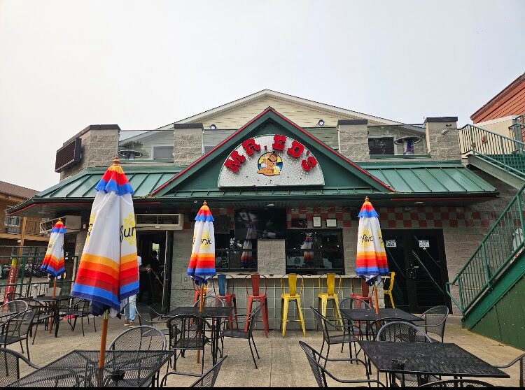Outdoor seating in front of a casual restaurant with colorful striped umbrellas and metal tables and chairs.