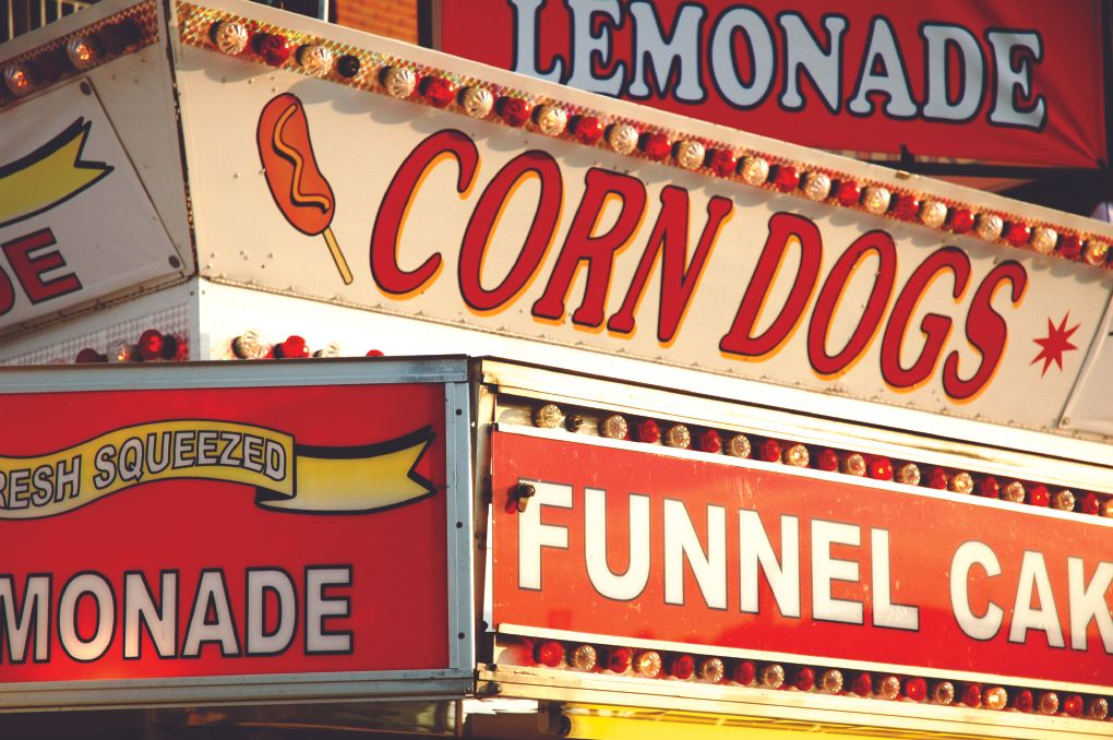 Bright carnival signs advertising lemonade, corn dogs and funnel cakes at a fairground booth