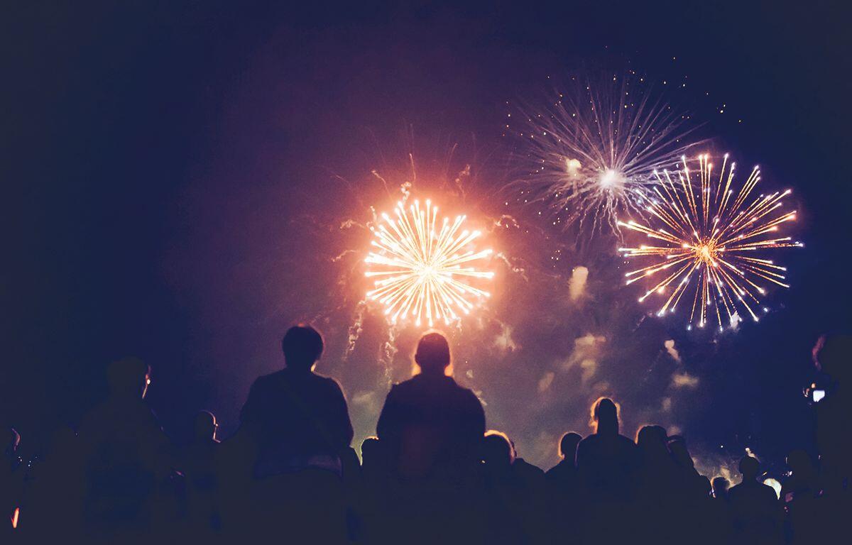 Silhouetted crowd watching bright fireworks explode in a dark night sky.