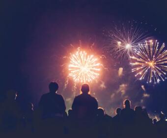 Silhouetted crowd watching bright fireworks explode in a dark night sky.