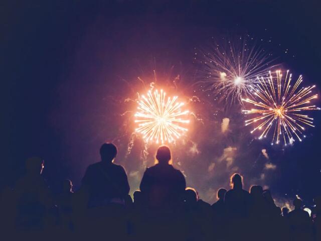 Silhouetted crowd watching bright fireworks explode in a dark night sky.