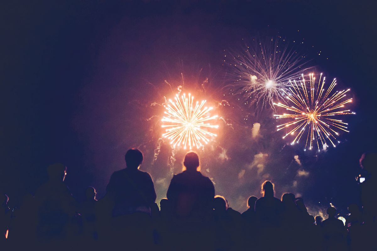 Silhouetted crowd watching bright fireworks explode in a dark night sky.