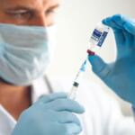 Healthcare worker in mask and blue gloves draws vaccine from a vial into a syringe text to administer a shot