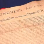 Close-up of an aged parchment showing the title 'In Congress, July 4, 1776' and 'Declaration of the United States of America'—a historical document scene.