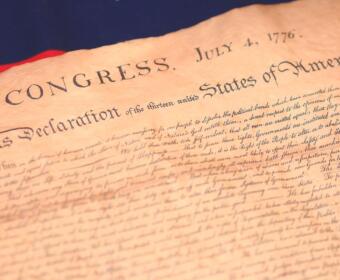 Close-up of an aged parchment showing the title 'In Congress, July 4, 1776' and 'Declaration of the United States of America'—a historical document scene.