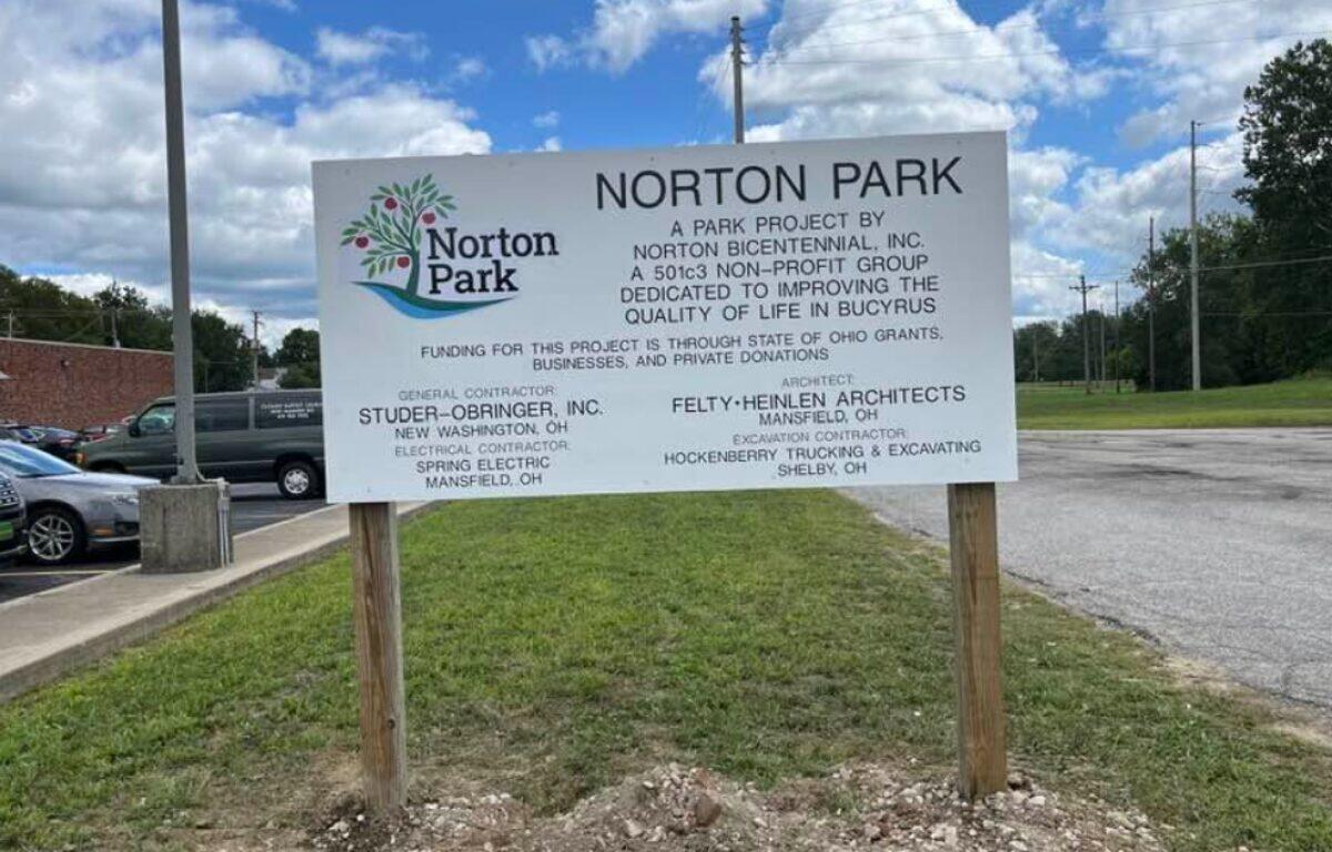 Norton Park sign listing park project sponsors and contractors, mounted on two wooden posts in a grassy lot.