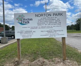 Norton Park sign listing park project sponsors and contractors, mounted on two wooden posts in a grassy lot.